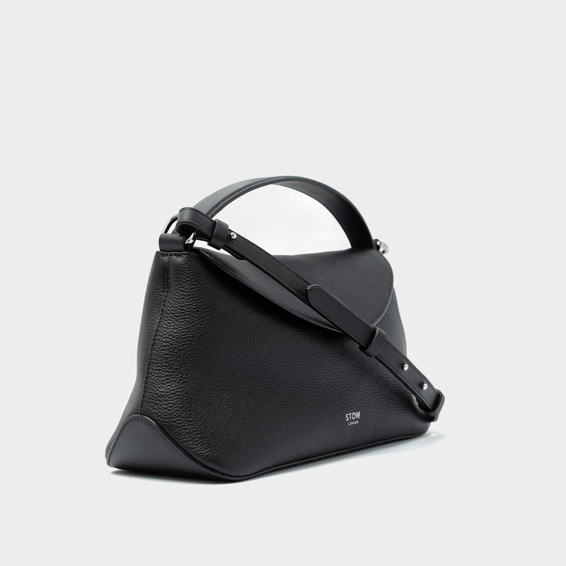 Side view of STOW London's East West in Black pebbled leather and detachable crossbody strap featuring silver stainless steel hardware on a light grey background