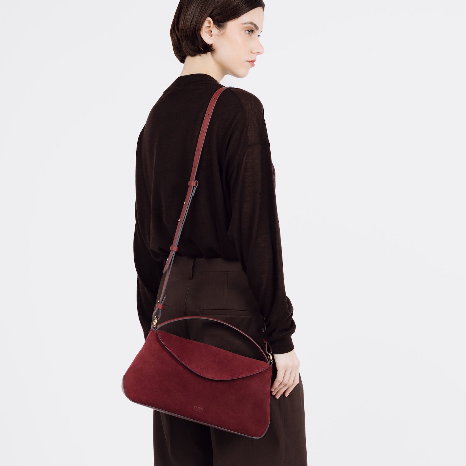 Model wearing STOW London's East West bag in Burgundy Suede leather over her shoulder featuring gold-coated stainless steel hardware on a white background