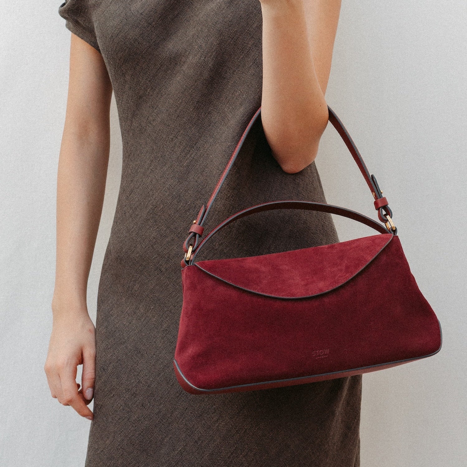 Model wearing STOW London's East West in Burgundy suede leather featuring the detachable shoulder strap with gold hardware