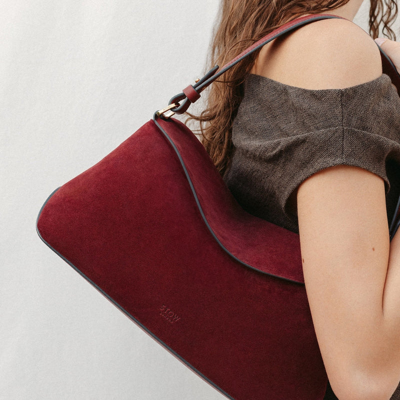 Model wearing STOW London's East West in Burgundy suede leather featuring the detachable shoulder strap with gold hardware