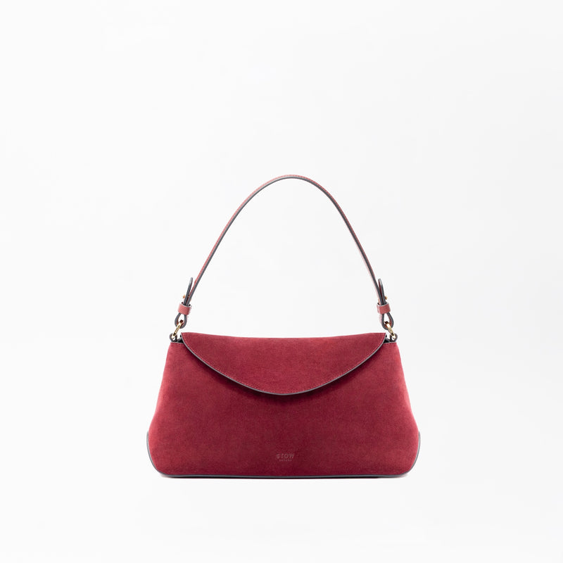 STOW London's East West in Burgundy suede leather on a light grey background featuring the detachable shoulder strap with gold hardware and details 