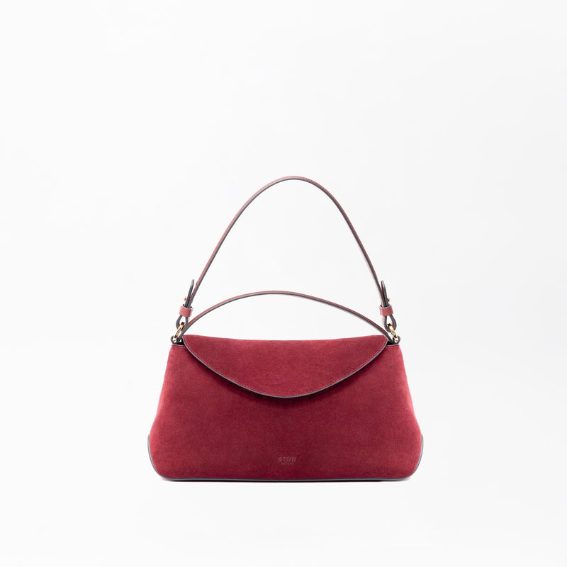 STOW London's East West in Burgundy suede leather on a light grey background featuring the detachable shoulder strap and top handle with gold hardware and details 
