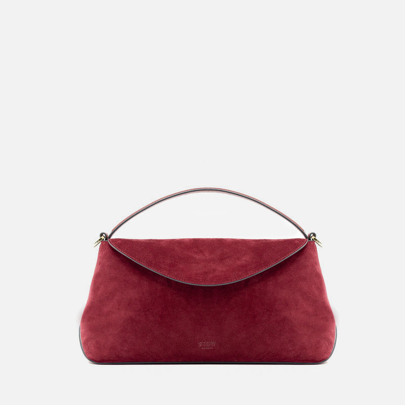 STOW London's East West in Burgundy suede leather featuring gold-coated stainless steel hardware on a light grey background