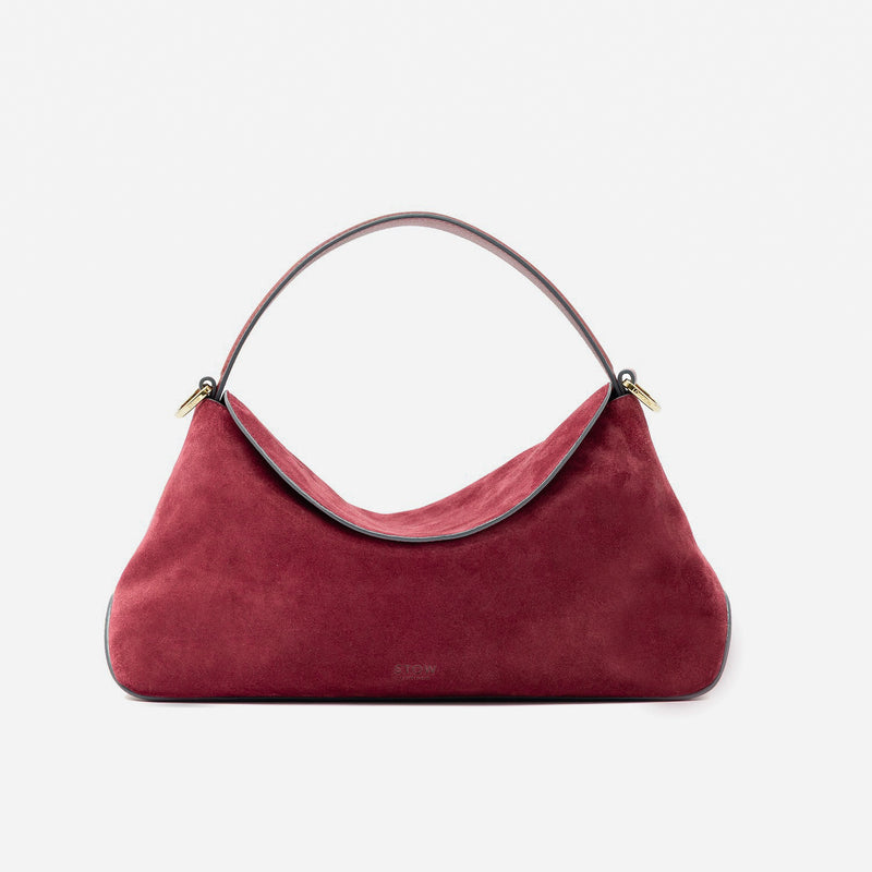 STOW London's East West in Burgundy suede leather featuring gold-coated stainless steel hardware on a light grey background