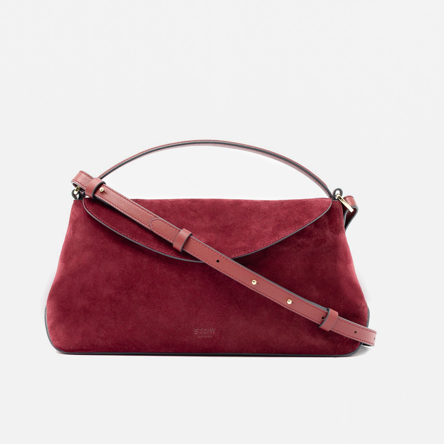 STOW London's East West in Burgundy suede leather and detachable crossbody strap featuring gold-coated stainless steel hardware on a light grey background