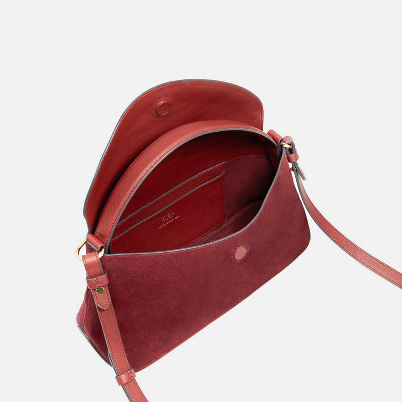 STOW London's East West in Burgundy suede leather with flap open showing suede interior and slip pocket featuring gold-coated stainless steel hardware on a light grey background