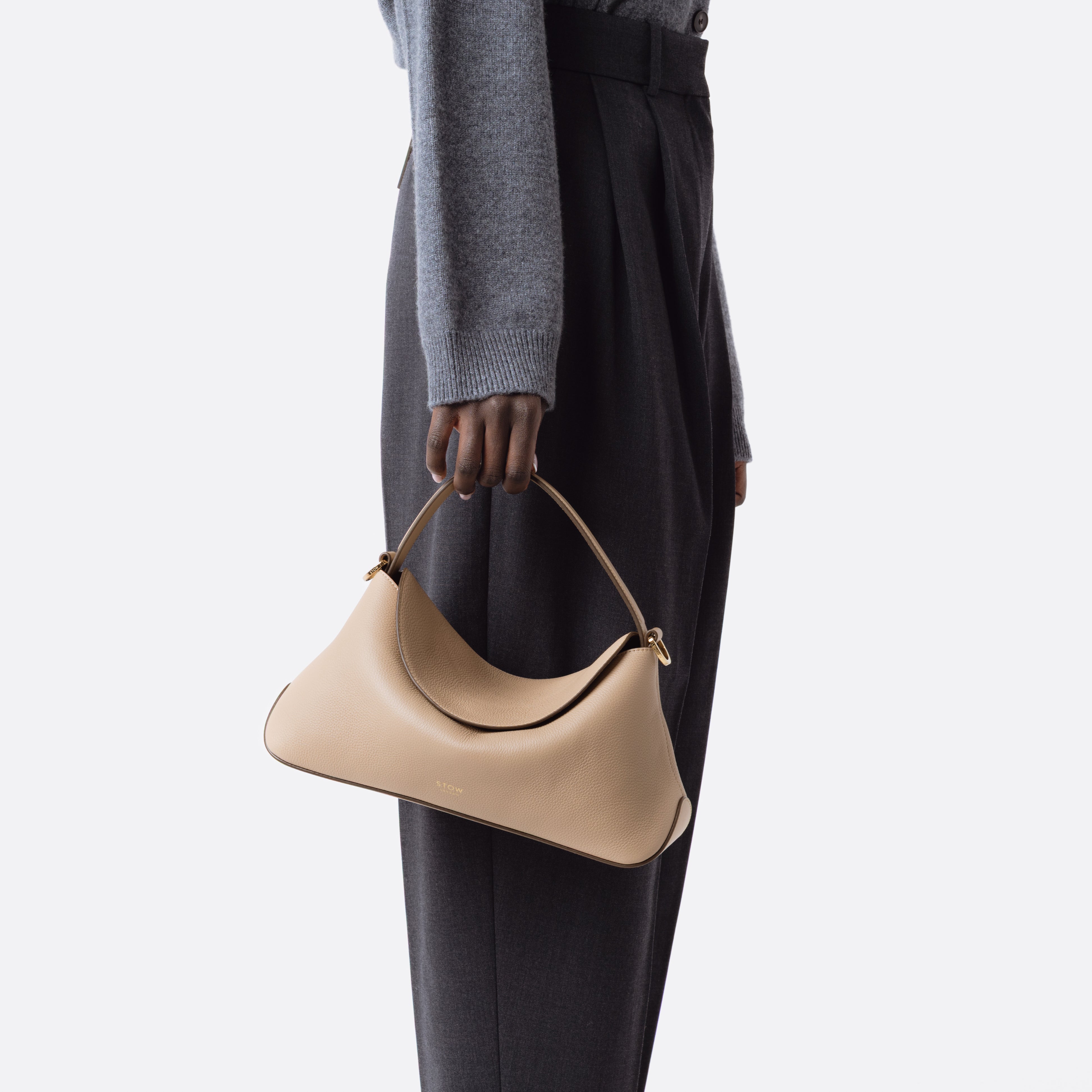 Model holding STOW London's East West in Camel pebbled leather at her side on a white background