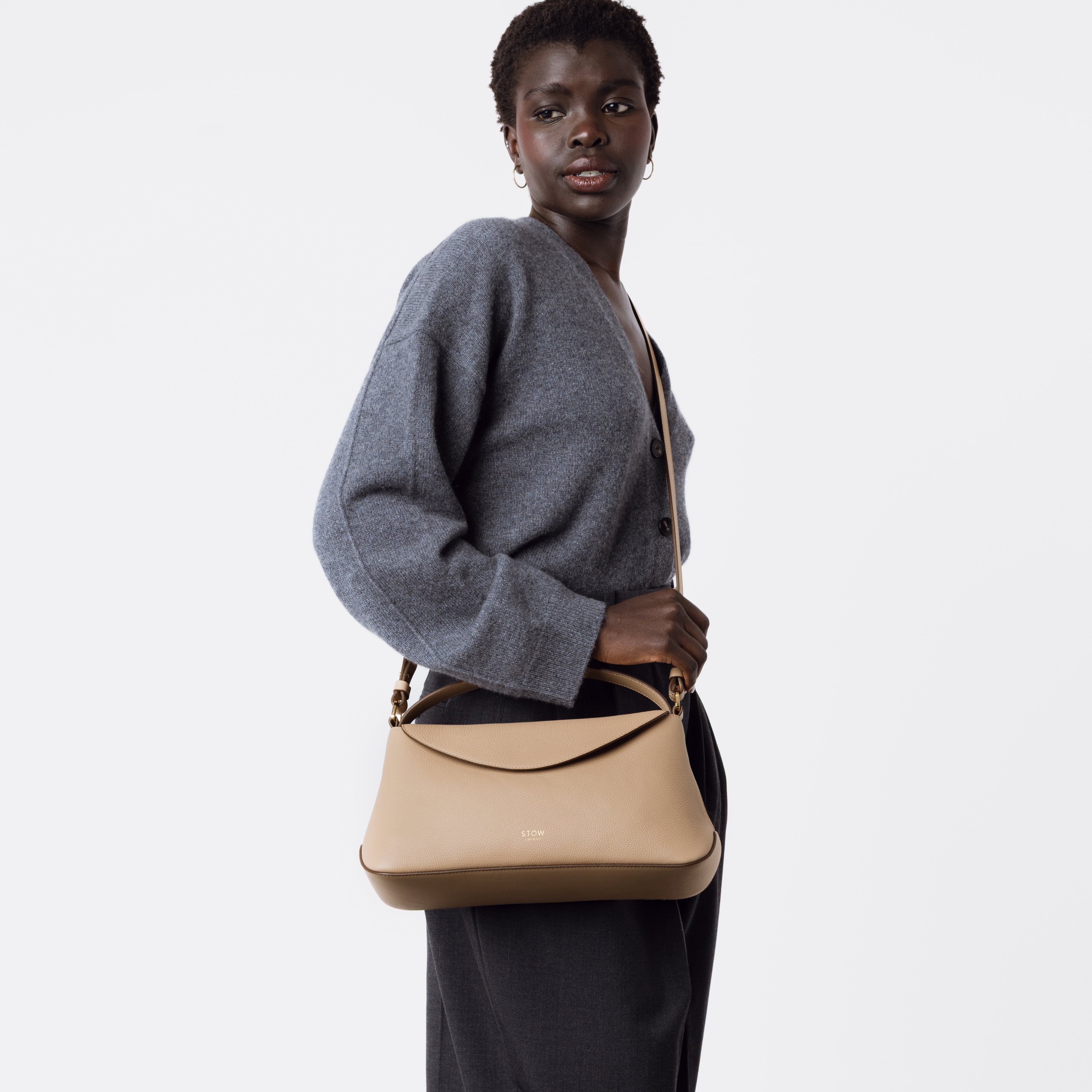 Model wearing STOW London's East West in Camel pebbled leather crossbody on a white background