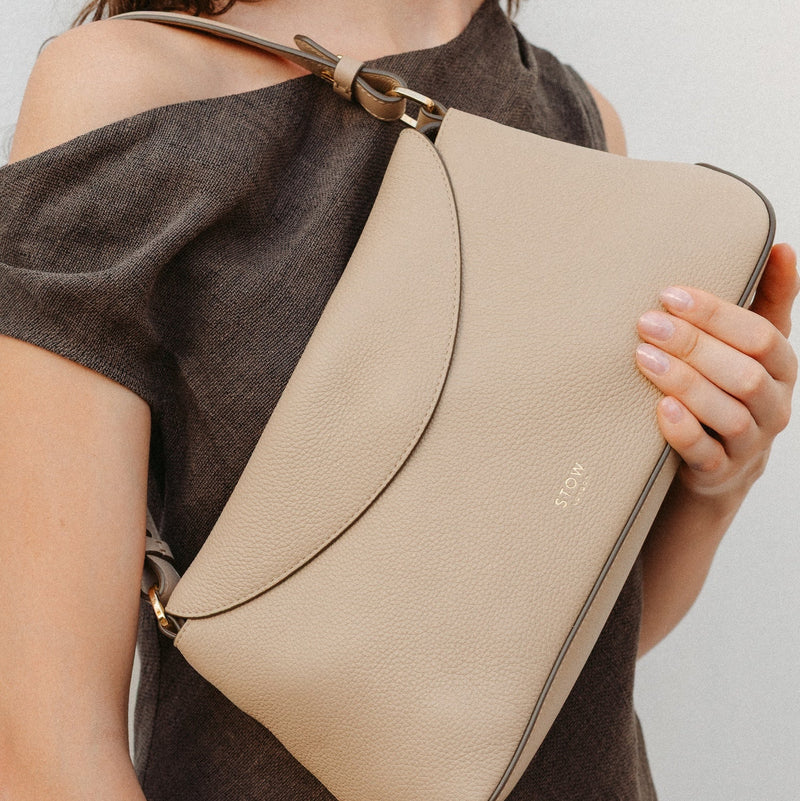 Model holding STOW London's East West in Camel leather featuring the detachable shoulder strap with gold hardware and details 