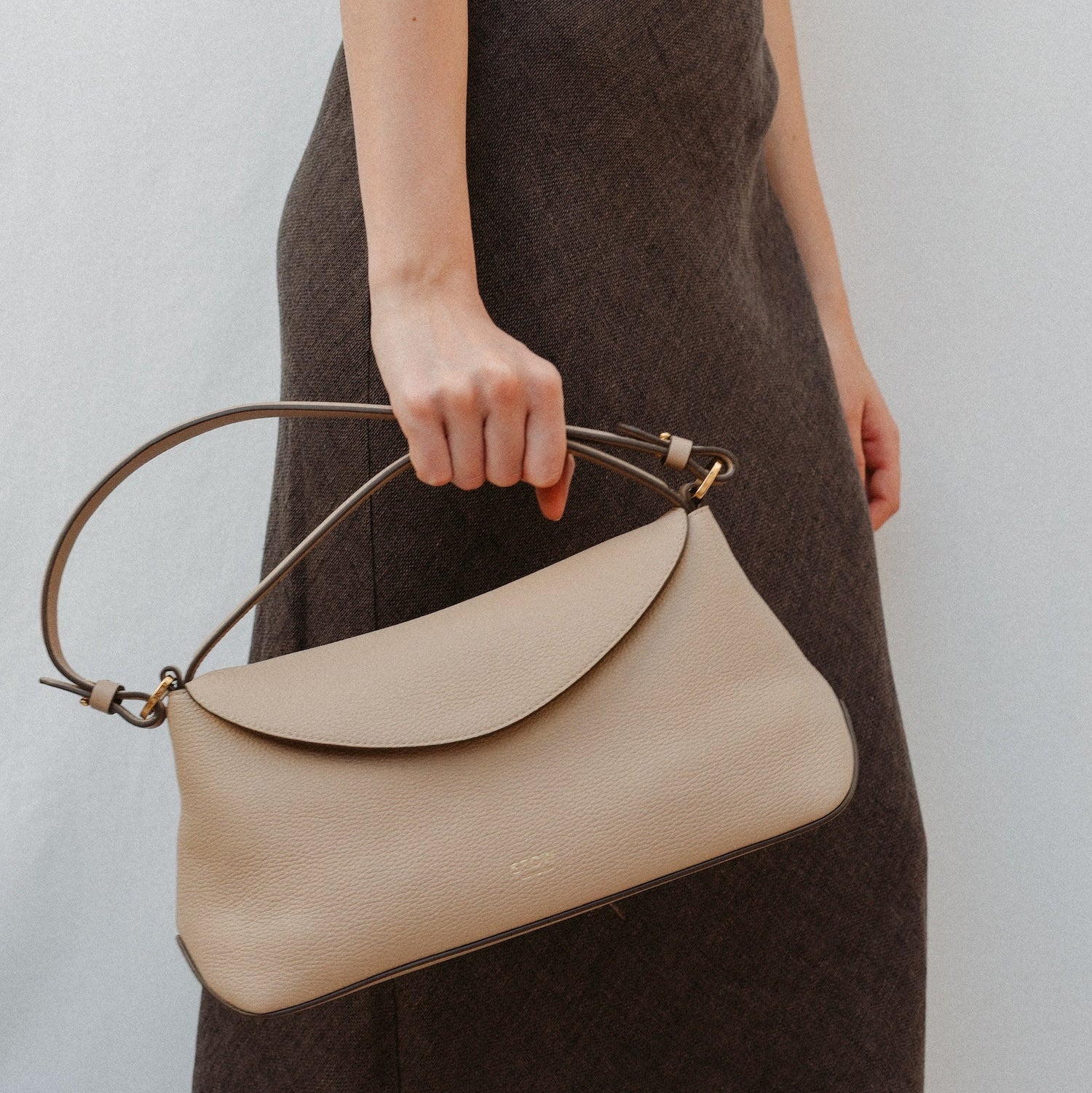 Model holding STOW London's East West in Camel leather featuring the detachable shoulder strap and top handle with gold hardware and details 