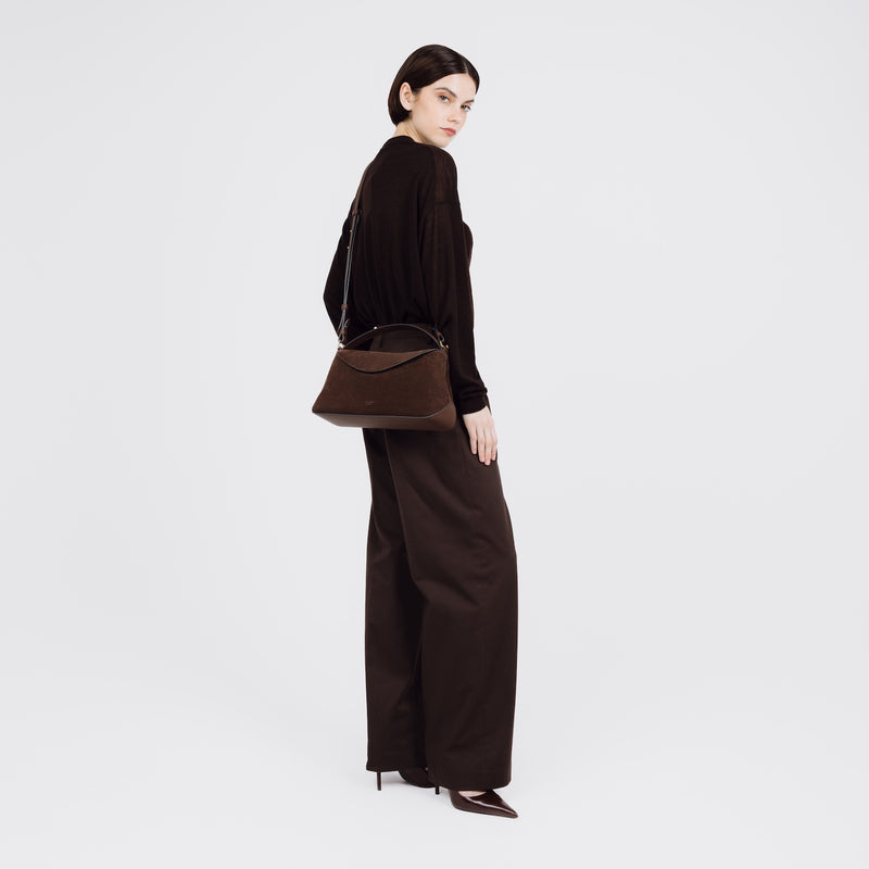 Model wearing STOW London's East West bag in Chocolate Suede leather crossbody featuring gold-coated stainless steel hardware on a white background