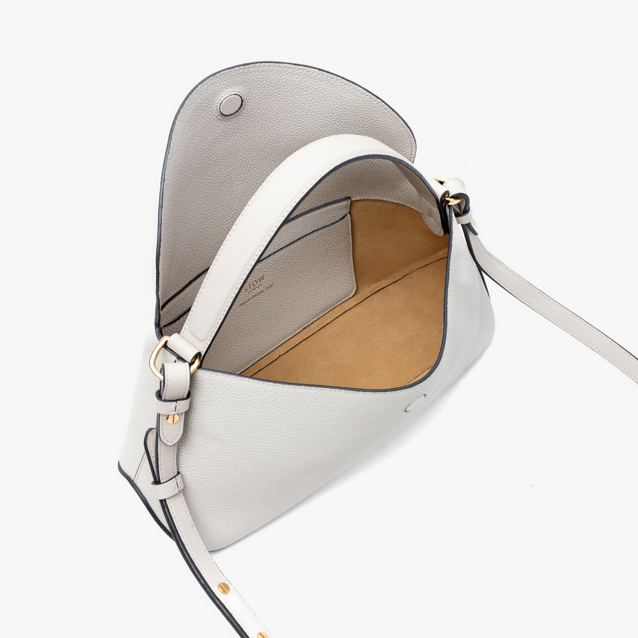 STOW London's East West in Cloud Grey pebbled leather with flap open showing light beige suede interior and slip pocket featuring gold-coated stainless steel hardware on a light grey background