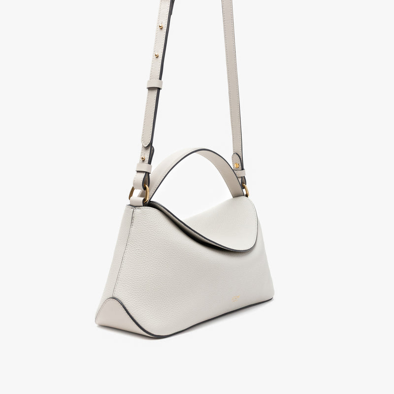 Off-axis view of STOW London's East West in Cloud Grey pebbled leather and detachable crossbody strap featuring gold-coated stainless steel hardware on a light grey background