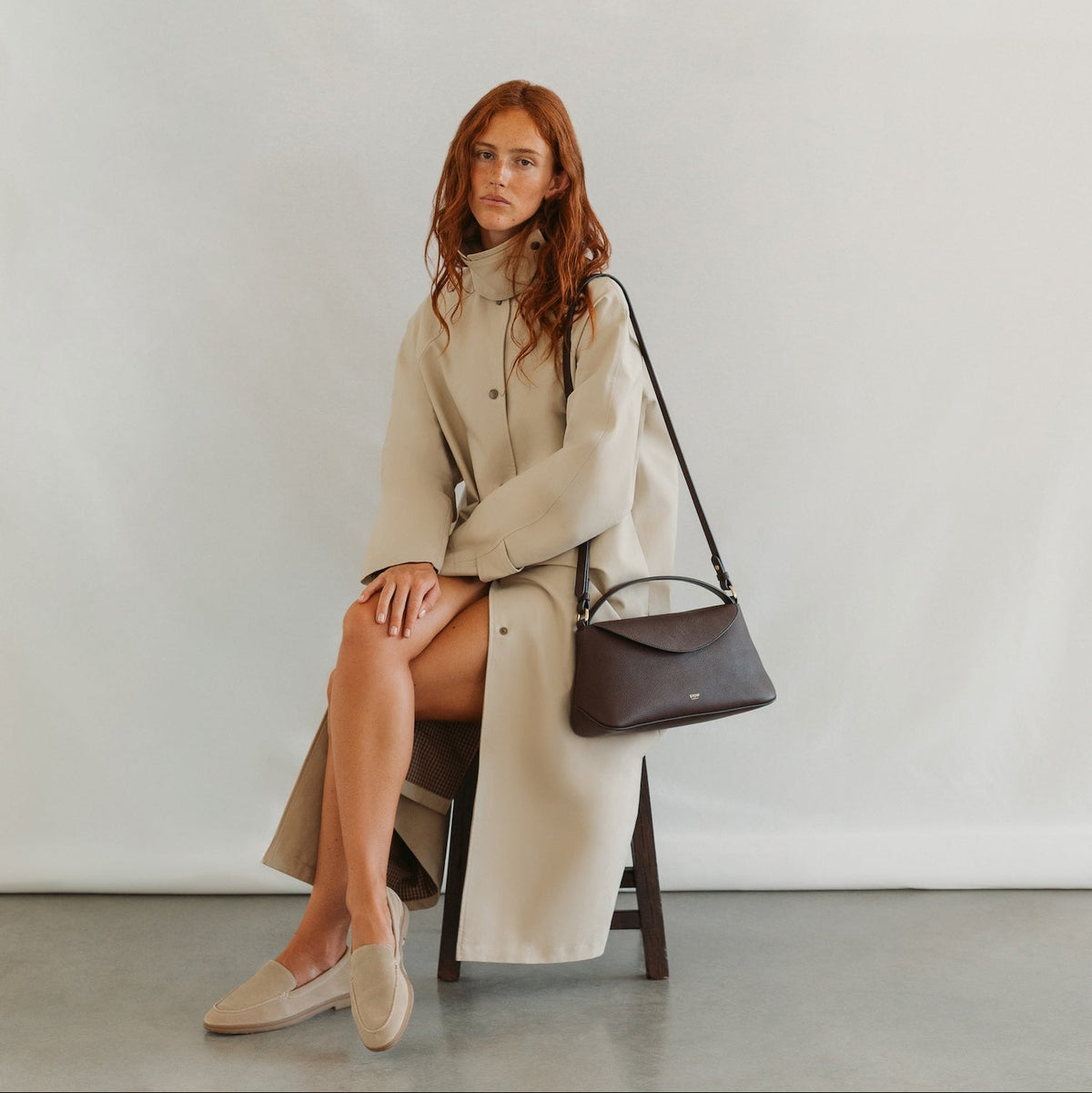 Model in a beige coat styling STOW London's East West in Espresso pebbled leather featuring gold-coated stainless steel hardware 