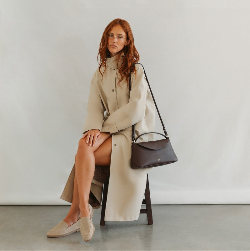 Model in a beige coat styling STOW London's East West in Espresso pebbled leather featuring gold-coated stainless steel hardware 