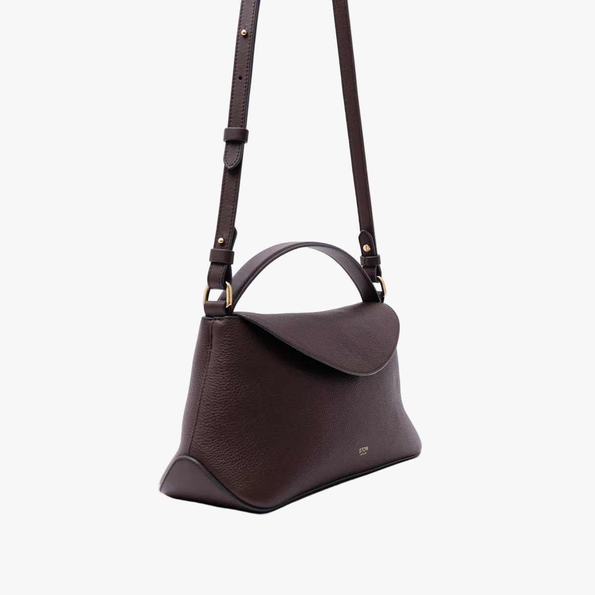 Off-axis view of STOW London's East West in Espresso pebbled leather on a light grey background featuring gold-coated stainless steel hardware and the detachable crossbody strap