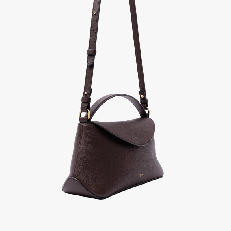 Off-axis view of STOW London's East West in Espresso pebbled leather on a light grey background featuring gold-coated stainless steel hardware and the detachable crossbody strap