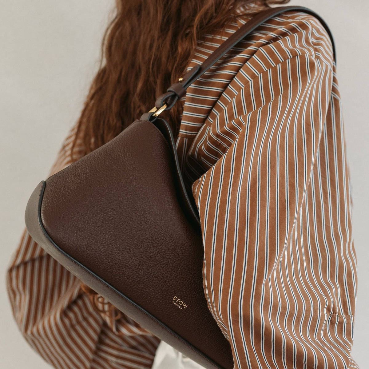 Model wearing STOW London's East West in Espresso pebbled leather featuring the detachable shoulder strap and gold-coated stainless steel hardware 