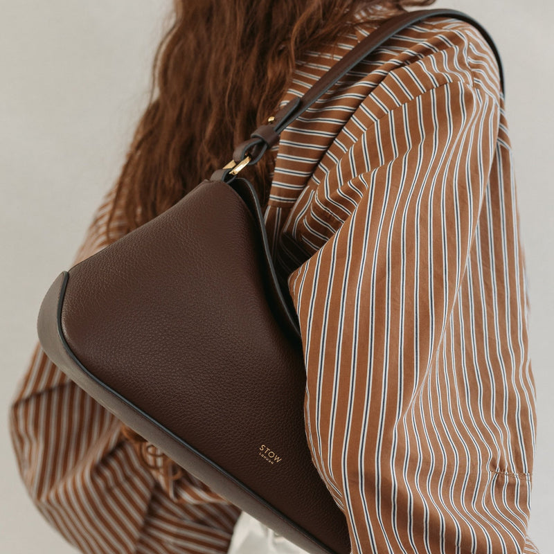 Model wearing STOW London's East West in Espresso pebbled leather featuring the detachable shoulder strap and gold-coated stainless steel hardware 