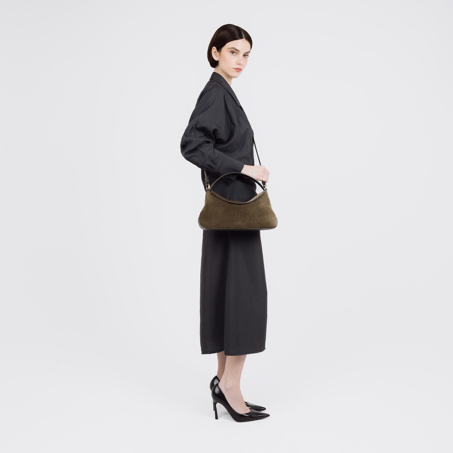 Model wearing STOW London's East West bag in Dark Green Suede leather crossbody featuring gold-coated stainless steel hardware on a white background