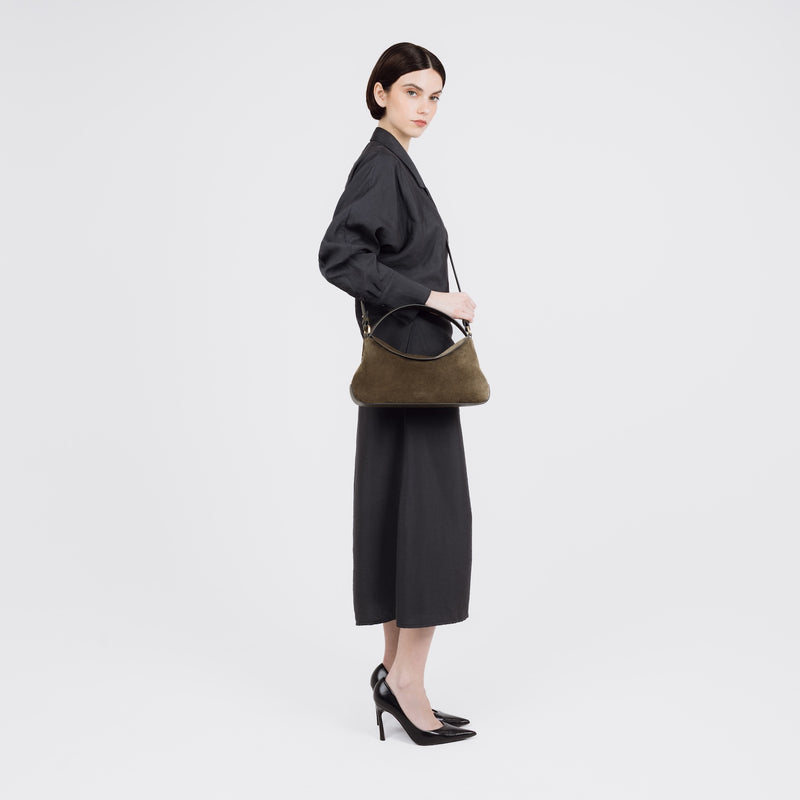 Model wearing STOW London's East West bag in Dark Green Suede leather crossbody featuring gold-coated stainless steel hardware on a white background