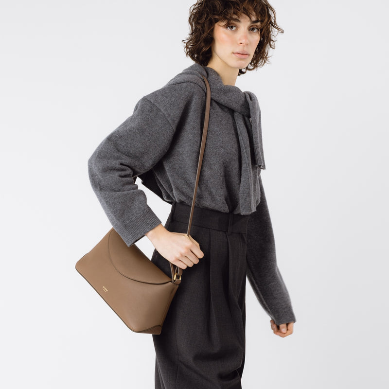 Model wearing STOW London's East West in Mocha leather on her shoulder featuring gold-coated stainless steel hardware on a white background