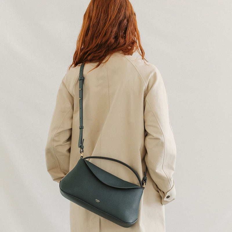 Model in a beige coat wearing STOW London's East West in New Forest pebbled leather crossbody featuring gold-coated stainless steel hardware 