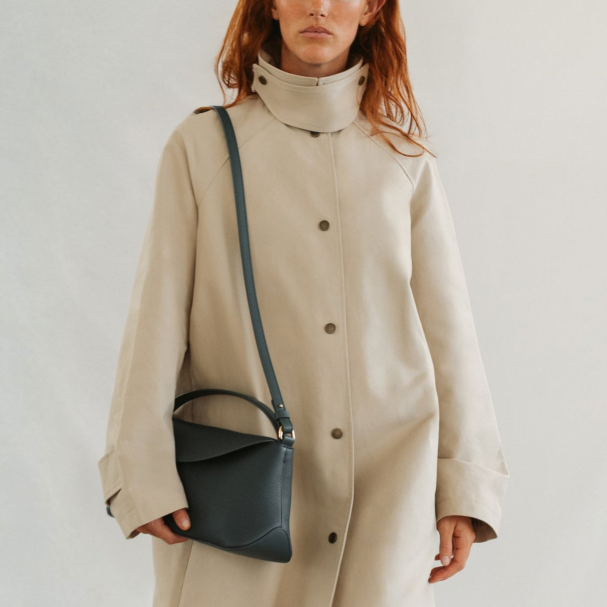 Model in a beige coat styling STOW London's East West in New Forest pebbled leather featuring gold-coated stainless steel hardware 