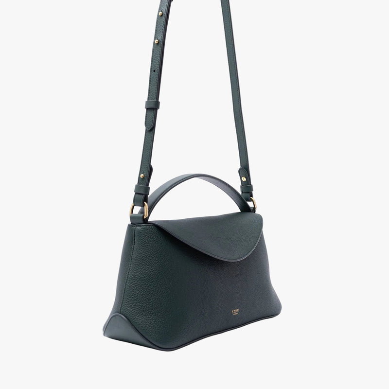 Off-axis view of STOW London's East West in New Forest pebbled leather on a light grey background featuring gold-coated stainless steel hardware and the detachable crossbody strap