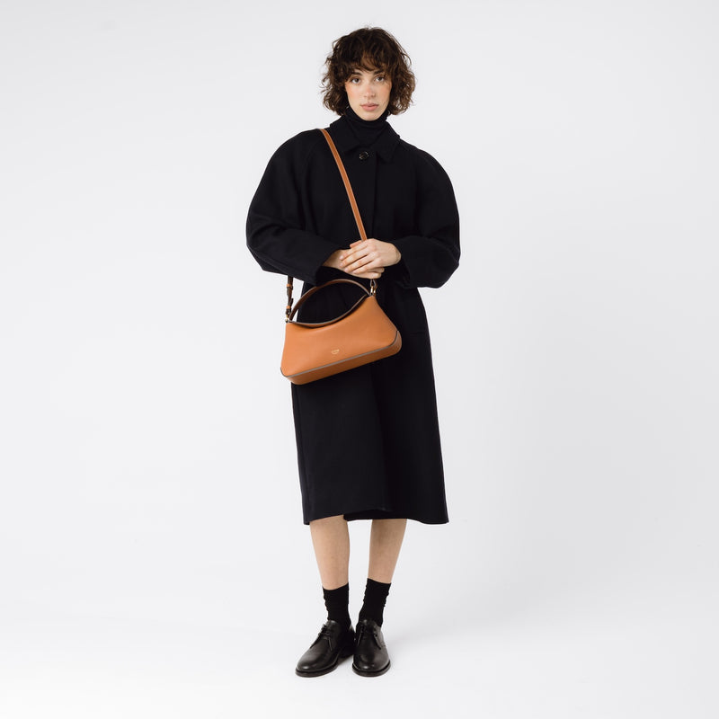 Model wearing STOW London's East West bag in Earth Tan on her shoulder featuring gold-coated stainless steel hardware on a white background