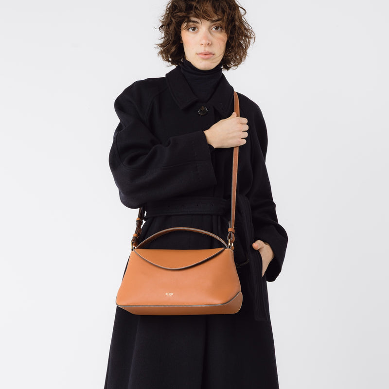 Model wearing STOW London's East West bag in Earth Tan crossbody featuring gold-coated stainless steel hardware on a white background