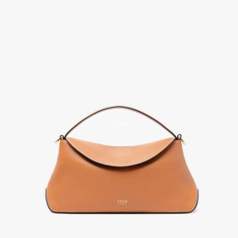STOW London's East West bag in Earth Tan pebbled leather featuring gold-coated stainless steel hardware on a light grey background