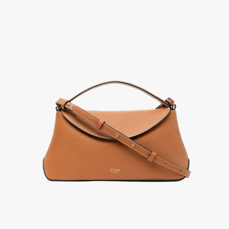 STOW London's East West bag in Earth Tan pebbled leather and crossbody strap featuring gold-coated stainless steel hardware on a light grey background