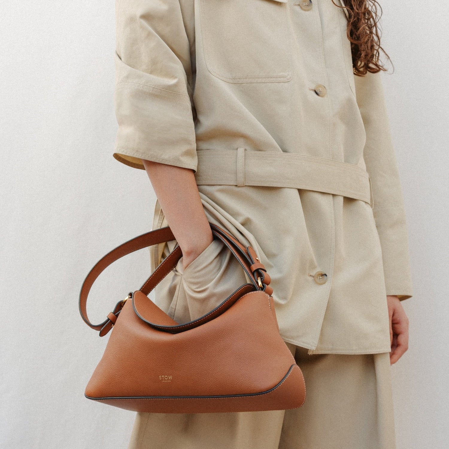 Model wearing STOW London's East West in Earth Tan leather featuring the detachable shoulder strap with gold hardware and details 