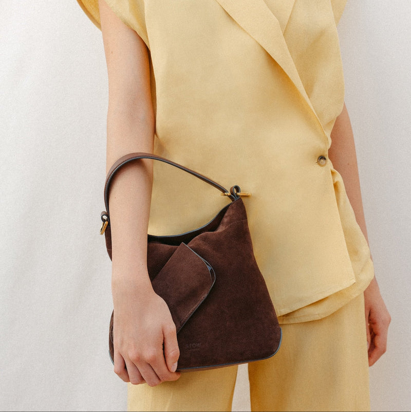 Model wearing a yellow outfit holding STOW London's Glasses Case and Midi Curve in Chocolate suede leather at her side