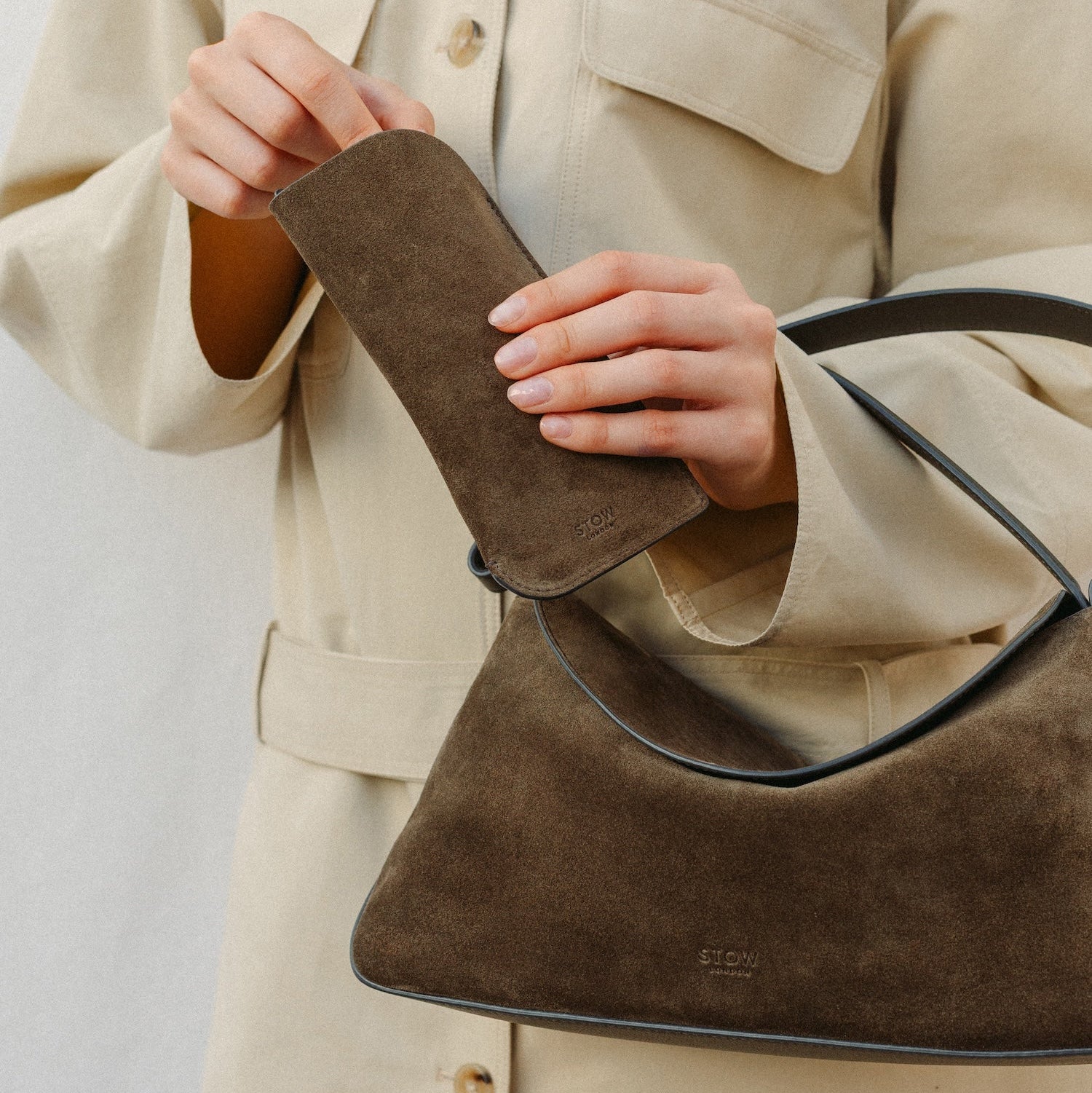 Model putting her glasses into STOW London's Glasses Case in Dark Green suede leather with the Dark Green suede East West on her arm 