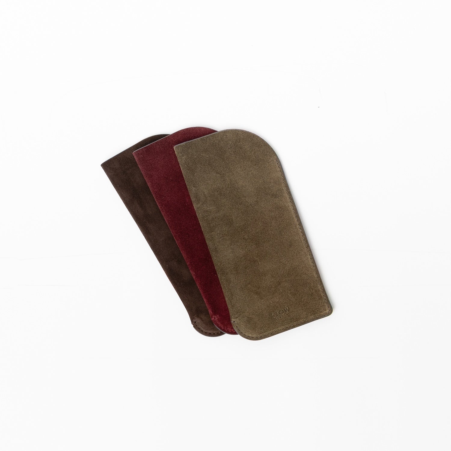 Shot of all three suede colours of STOW London's Glasses Case on a light grey background featuring an embossed STOW London on the front