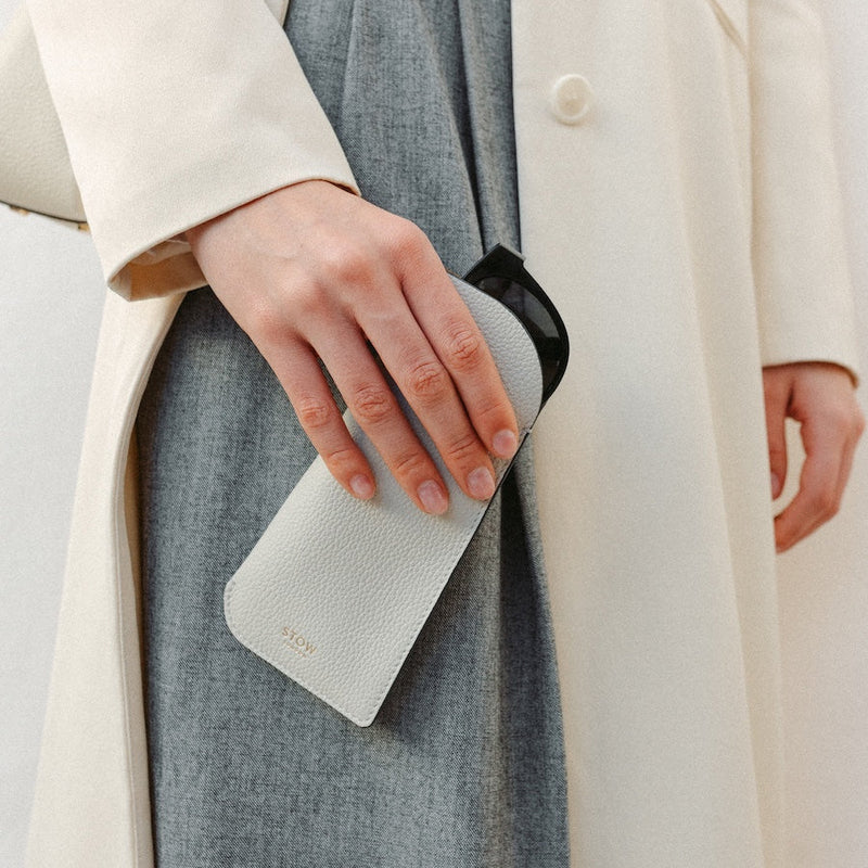 Model holding STOW London's Glasses Case in Cloud Grey pebbled leather, featuring a gold logo