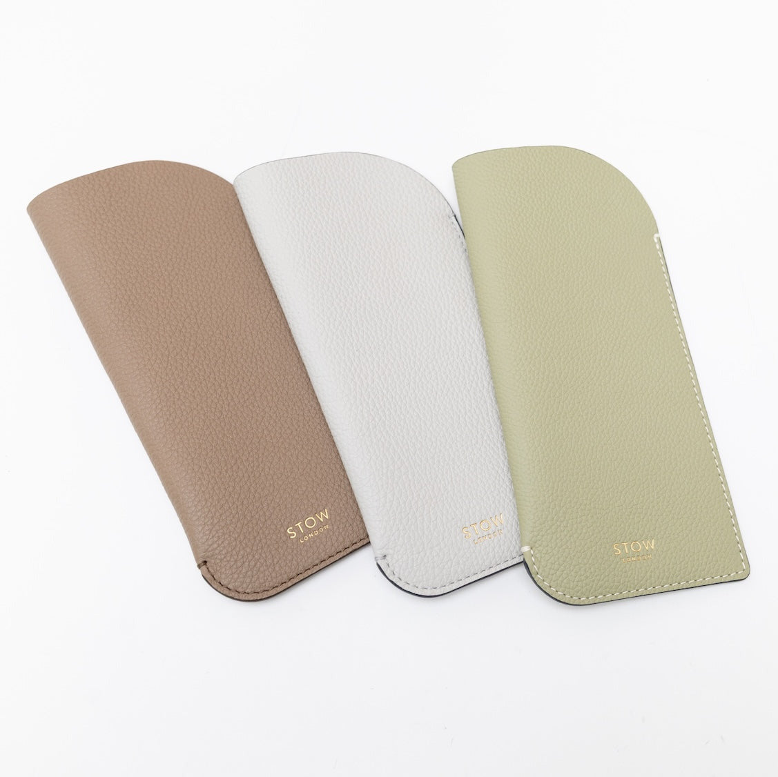 Shot of all three pebbled leather colours of STOW London's Glasses Case featuring gold logos on a white background