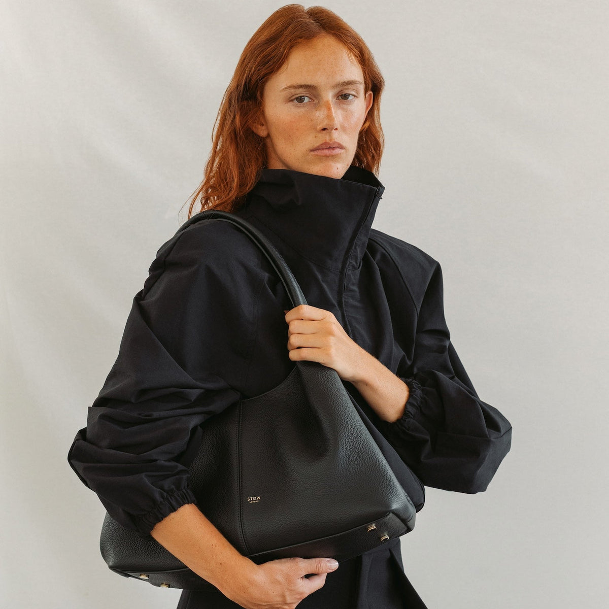 Model wearing STOW London's Hobo Tote in Black pebbled leather featuring a pleated front panel and gold-coated stainless steel hardware 