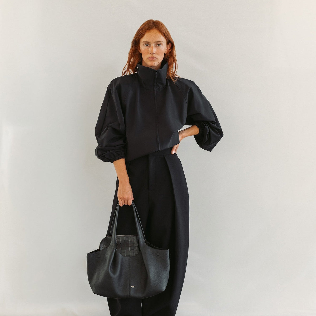 Model holding STOW London's Hobo Tote in Black pebbled leather featuring a pleated front panel and gold-coated stainless steel hardware 