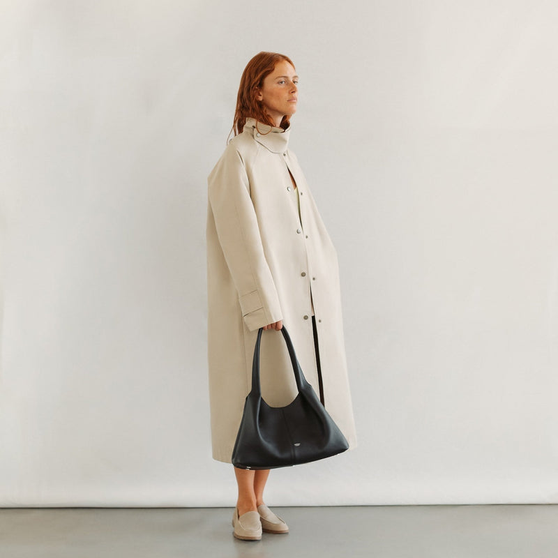 Model holding STOW London's Hobo Tote in Black pebbled leather featuring a pleated front panel and silver base feet 