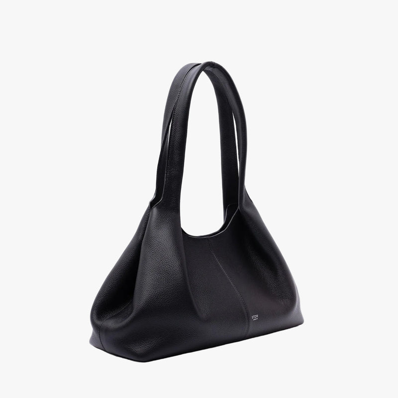 Off-axis view of STOW London's Hobo Tote in Black pebbled leather in its triangular hobo bag shape on a light grey background featuring a pleated front panel and small silver embossed logo