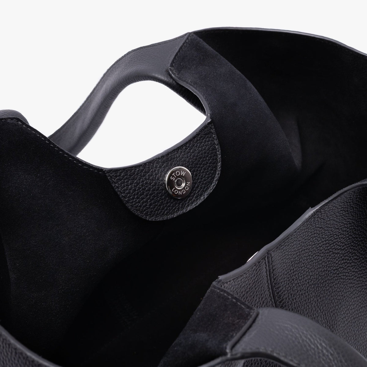 Close up of the black suede interior lining and silver magnetic closure on STOW London's Hobo Tote in Black pebbled leather on a light grey background 
