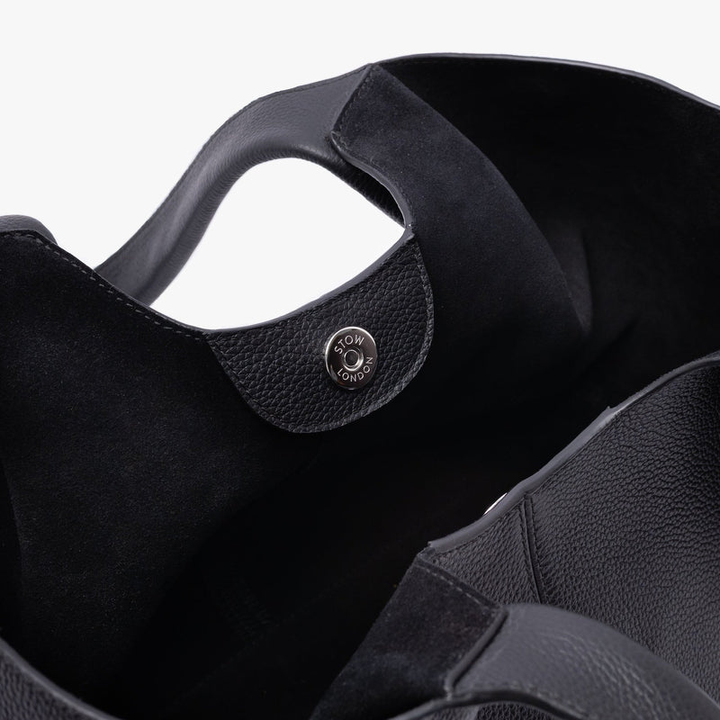 Close up of the black suede interior lining and silver magnetic closure on STOW London's Hobo Tote in Black pebbled leather on a light grey background 