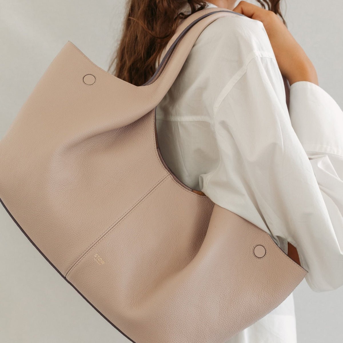 Model wearing STOW London's Hobo Tote in Camel pebbled leather featuring a pleated front panel and gold-coated stainless steel hardware 