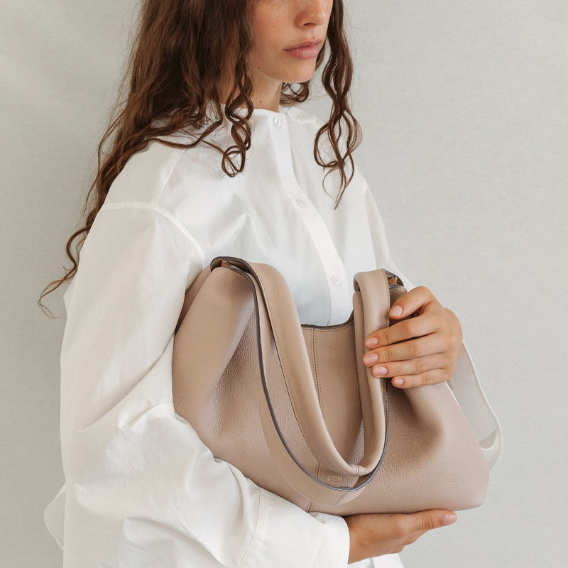 Model with STOW London's Hobo Tote in Camel pebbled leather featuring a pleated front panel and gold-coated stainless steel hardware 