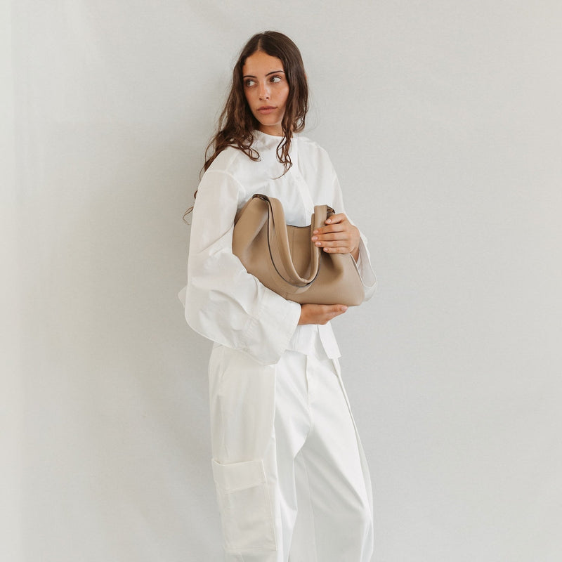 Model holding STOW London's Hobo Tote in Camel pebbled leather featuring a pleated front panel and gold-coated stainless steel hardware 