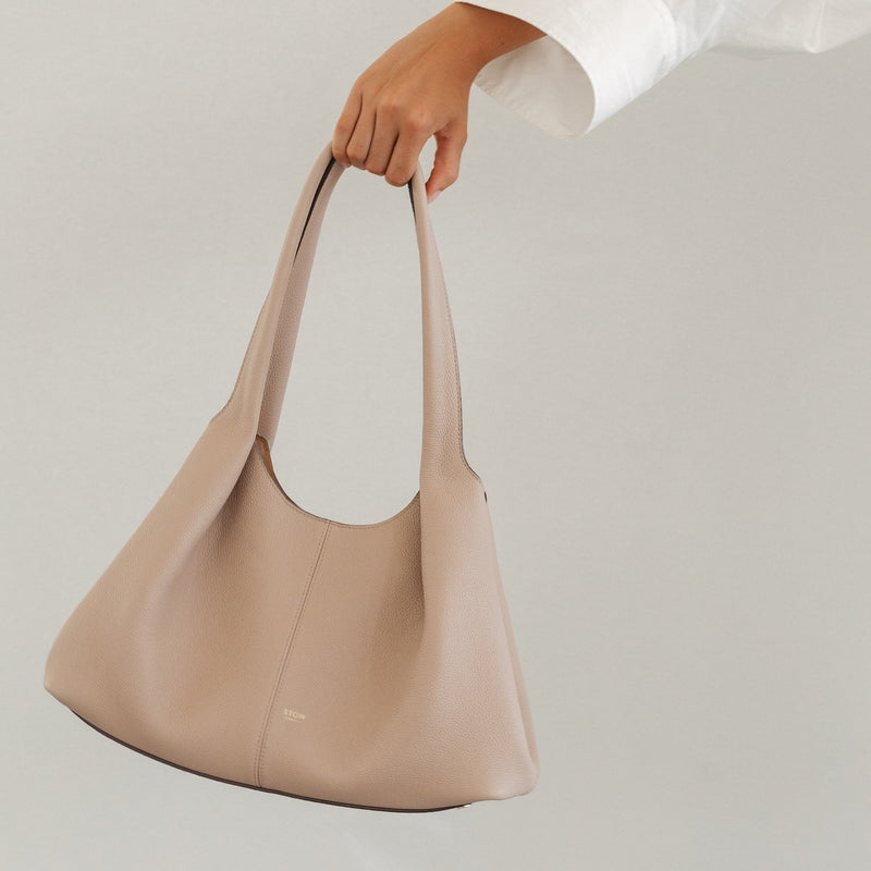 Model holding STOW London's Hobo Tote in Camel pebbled leather featuring a pleated front panel and gold-coated stainless steel hardware 