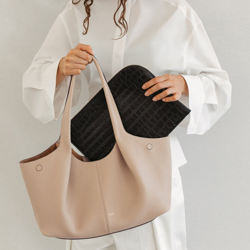 Model with STOW London's Hobo Tote in Camel pebbled leather inserting the Midi Leather Sleeve in Black Embossed Croc leather featuring a pleated front panel and gold-coated stainless steel hardware 